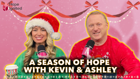 Ashley and Kevin smile at their microphones in Christmas attire.